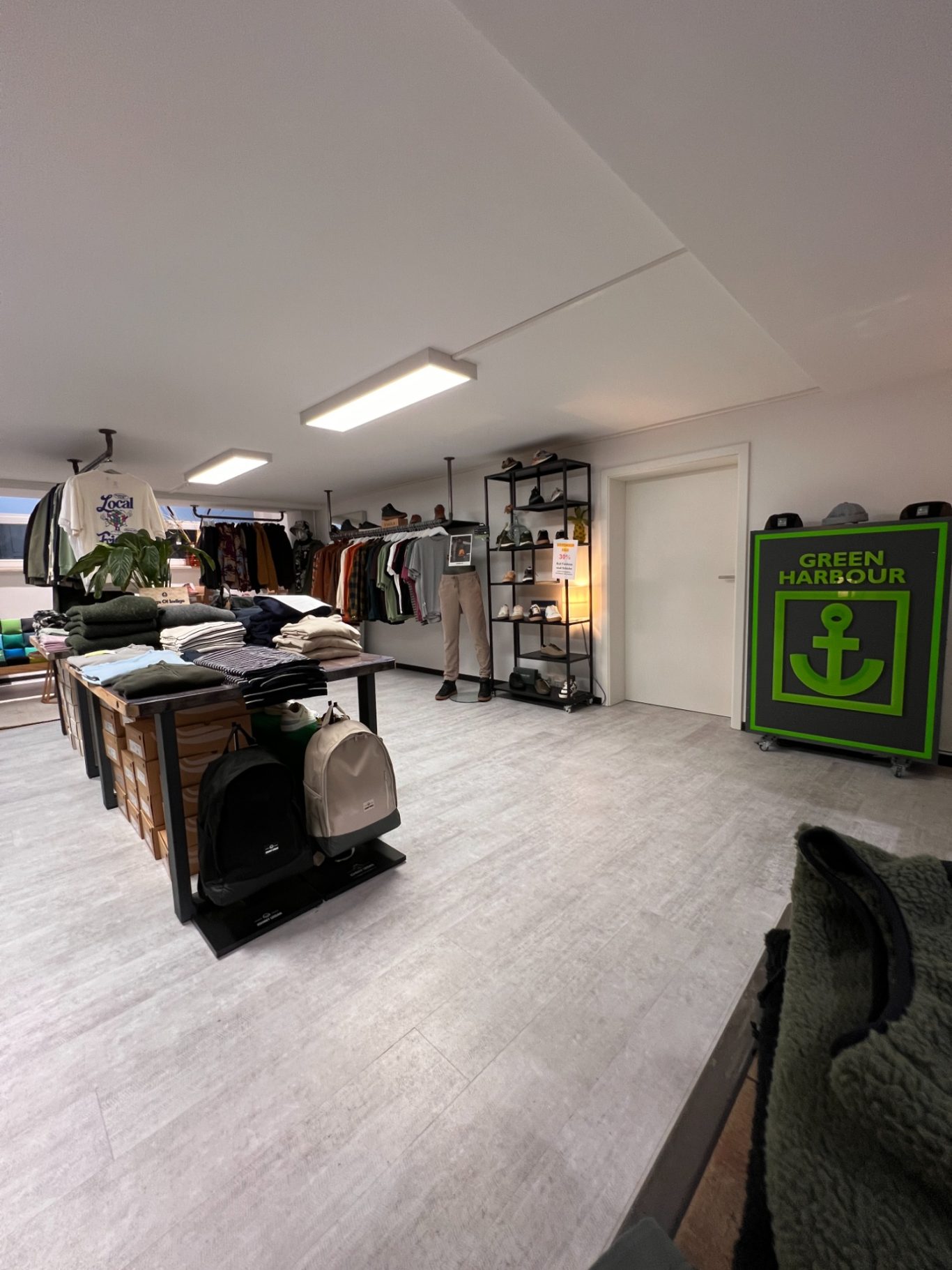Ein moderner Laden mit Kleidung, Regalen und einem grünen Ankermotiv.